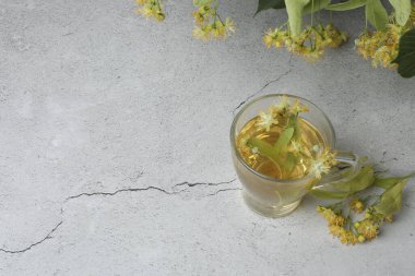 Ahşap zemin üzerinde ıhlamur çiçekleri olan bir fincan bitki çayı.