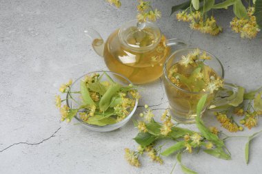 Ahşap zemin üzerinde ıhlamur çiçekleri olan bir fincan bitki çayı.