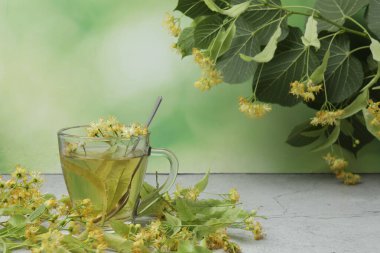 Ahşap zemin üzerinde ıhlamur çiçekleri olan bir fincan bitki çayı.