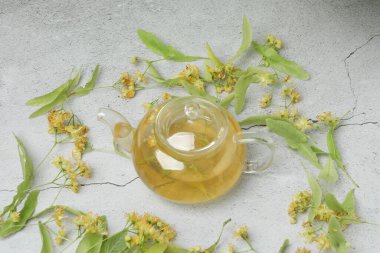 Ahşap zemin üzerinde ıhlamur çiçekleri olan bir fincan bitki çayı.