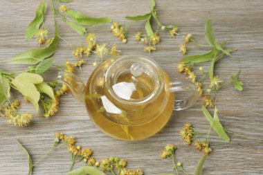 Ahşap zemin üzerinde ıhlamur çiçekleri olan bir fincan bitki çayı.