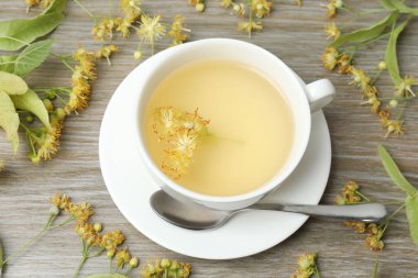 Ahşap zemin üzerinde ıhlamur çiçekleri olan bir fincan bitki çayı.