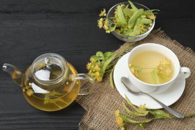 Ahşap zemin üzerinde ıhlamur çiçekleri olan bir fincan bitki çayı.