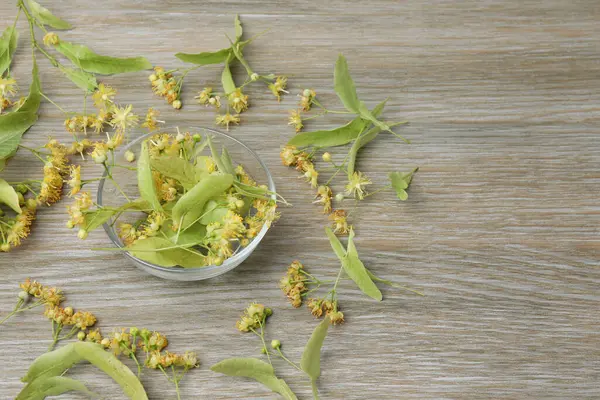 Ahşap zemin üzerinde ıhlamur çiçekleri olan bir fincan bitki çayı.