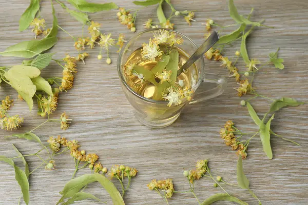 Ahşap zemin üzerinde ıhlamur çiçekleri olan bir fincan bitki çayı.