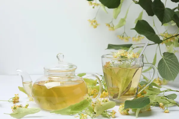 Ahşap zemin üzerinde ıhlamur çiçekleri olan bir fincan bitki çayı.