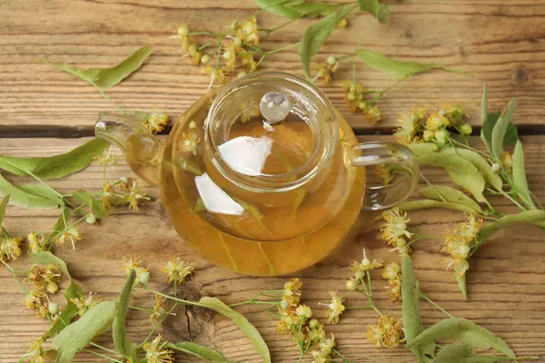 Ahşap zemin üzerinde ıhlamur çiçekleri olan bir fincan bitki çayı.