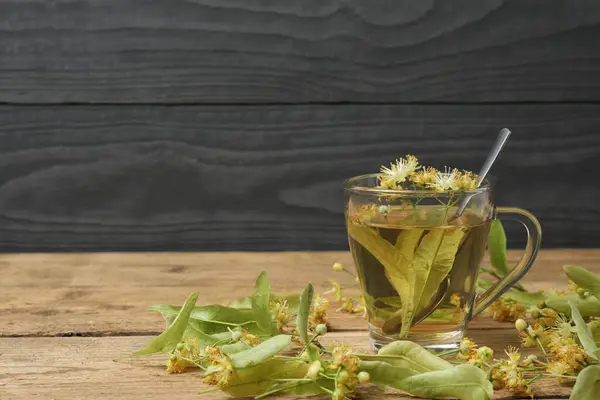 Ahşap zemin üzerinde ıhlamur çiçekleri olan bir fincan bitki çayı.