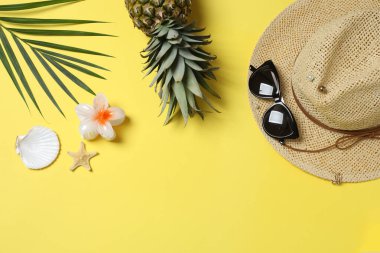 Yukarıdan gelen tropik titreşimler. Hasır şapka, güneş gözlüğü, ananas, hasır çanta, sarı arka planda plaj aksesuarları. Reklam ya da metin kaplamaları için mükemmel