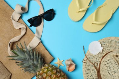 Yukarıdan gelen tropik titreşimler. Hasır şapka, güneş gözlüğü, ananas, hasır çanta, mavi arka planda plaj aksesuarları. Reklam ya da metin kaplamaları için mükemmel