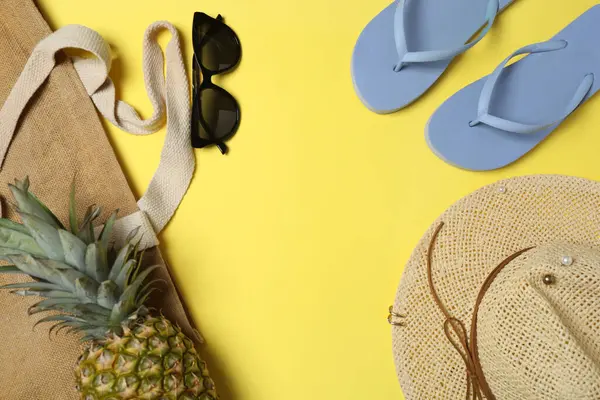 Yukarıdan gelen tropik titreşimler. Hasır şapka, güneş gözlüğü, ananas, hasır çanta, sarı arka planda plaj aksesuarları. Reklam ya da metin kaplamaları için mükemmel