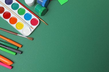 Okul malzemelerinin, kalemlerin, silgilerin, ataçların ve defterlerin yeşil arka planda üst görüntüsü. Eğitimle ilgili konular için ideal resim,