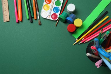 Okul malzemelerinin, kalemlerin, silgilerin, ataçların ve defterlerin yeşil arka planda üst görüntüsü. Eğitimle ilgili konular için ideal resim,