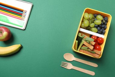 Atıştırmalık, meyve, sebze ve suyla birlikte yeşil arka planda okul malzemeleri.