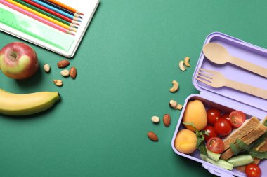 Atıştırmalık, meyve, sebze ve suyla birlikte yeşil arka planda okul malzemeleri.