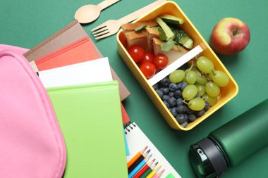 Atıştırmalık, meyve, sebze ve suyla birlikte yeşil arka planda okul malzemeleri.