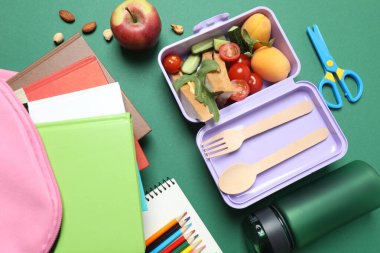 Atıştırmalık, meyve, sebze ve suyla birlikte yeşil arka planda okul malzemeleri.