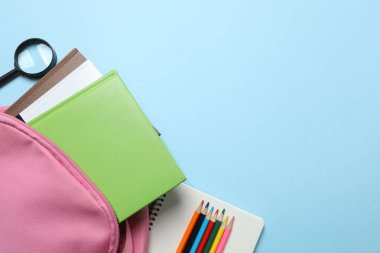 Abur cubur, meyve, sebze ve su ile beslenme çantasının yanı sıra mavi arka planda okul malzemeleri.