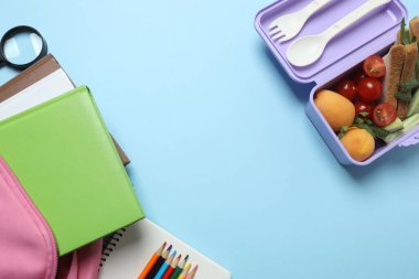 Abur cubur, meyve, sebze ve su ile beslenme çantasının yanı sıra mavi arka planda okul malzemeleri.