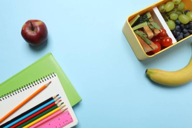 Abur cubur, meyve, sebze ve su ile beslenme çantasının yanı sıra mavi arka planda okul malzemeleri.