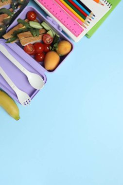 Abur cubur, meyve, sebze ve su ile beslenme çantasının yanı sıra mavi arka planda okul malzemeleri.