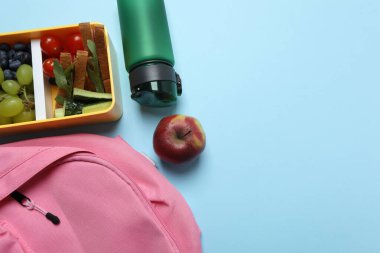 Abur cubur, meyve, sebze ve su ile beslenme çantasının yanı sıra mavi arka planda okul malzemeleri.