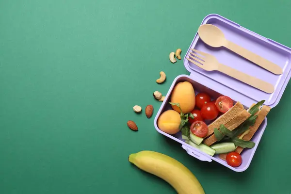 Atıştırmalık, meyve, sebze ve suyla birlikte yeşil arka planda okul malzemeleri.