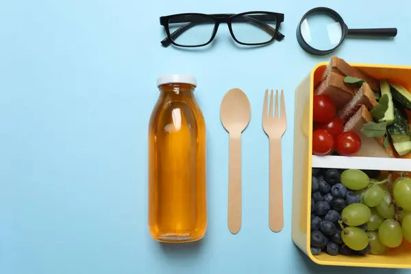 Abur cubur, meyve, sebze ve su ile beslenme çantasının yanı sıra mavi arka planda okul malzemeleri.