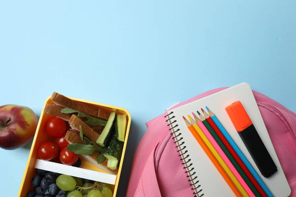 lunchbox with snacks, fruits, vegetables and water, as well as school supplies on a blue background