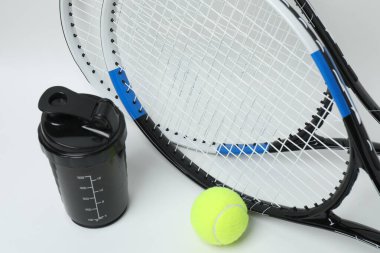 Tenis raketi, spor şişesi ve beyaz arka planda top.