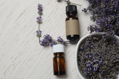 Lavanta yağlı şişeler, beyaz ahşap arka planda lavantalar.