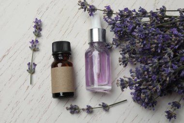 Lavanta yağlı şişeler, beyaz ahşap arka planda lavantalar.