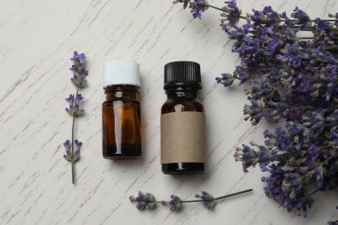 Lavanta yağlı şişeler, beyaz ahşap arka planda lavantalar.