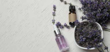 Açık gri arka planda lavanta yağı ve lavanta çiçekleri.