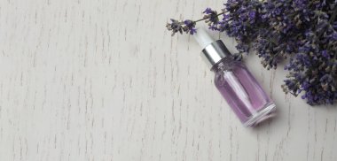 Beyaz arka planda lavanta çiçekleri olan lavanta yağı şişede, düz yerde.