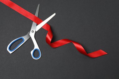 Siyah arkaplanda kırmızı kurdele ve makas.