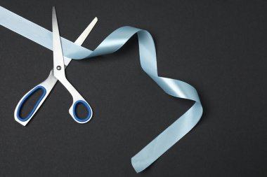 Siyah arka planda mavi kurdele ve makas, düz tasarım. Metin için yer.