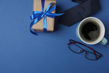 Babalar Günü. Hediye kutusu, bardak, kahve fincanı ve koyu mavi arka planda kravat..