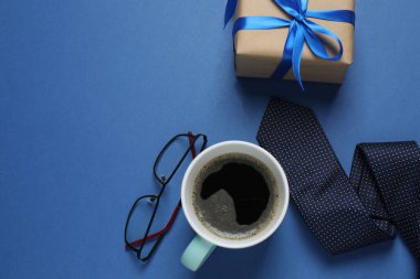 Babalar Günü. Hediye kutusu, bardak, kahve fincanı ve koyu mavi arka planda kravat..