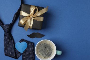 Babalar Günü. Hediye kutusu, bardak, kahve fincanı ve koyu mavi arka planda kravat..