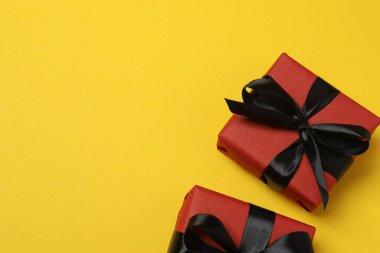 Sarı arka planda siyah kurdeleli kırmızı hediye kutuları.