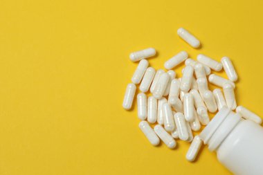 Sarı arka planda vitamin hapları ve şişe, üst manzara. Metin için boşluk