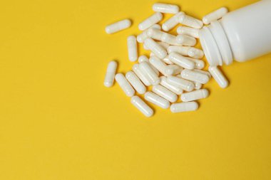Sarı arka planda vitamin hapları ve şişe, üst manzara. Metin için boşluk