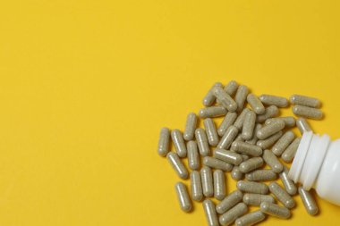 Sarı arka planda vitamin hapları ve şişe, üst manzara. Metin için boşluk