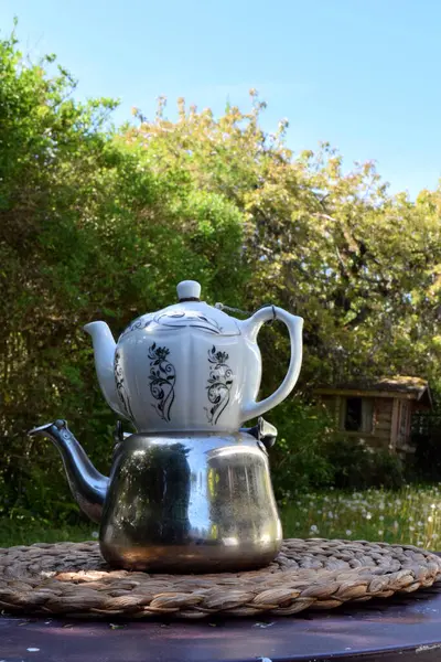 Bereketli bir yeşillik ve rahat bir arka bahçe atmosferiyle çevrili kırsal bir masada güzel hazırlanmış bir çaydanlık içeren sakin bir açık hava çay seti..  