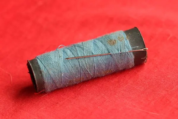 Kırmızı bir arkaplana yerleştirilmiş, iğneli mavi bir makara.