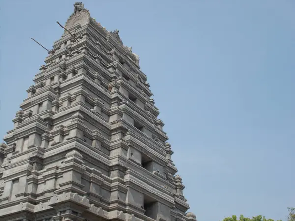            Açık mavi gökyüzüne doğru yükselen çok katmanlı taş tapınak kulesinin (gopuram) alçak açılı görüntüsü, Güney Hindistan tapınağının karakteristik piramit yapısını gözler önüne seriyor..