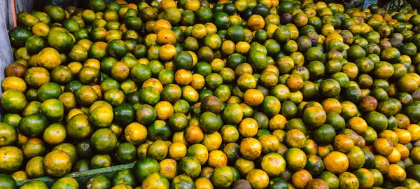  Büyük bir yeşil ve sarı portakal yığınına yakın çekim, bir pazarda veya meyve standında taze ürünler sergileniyor.