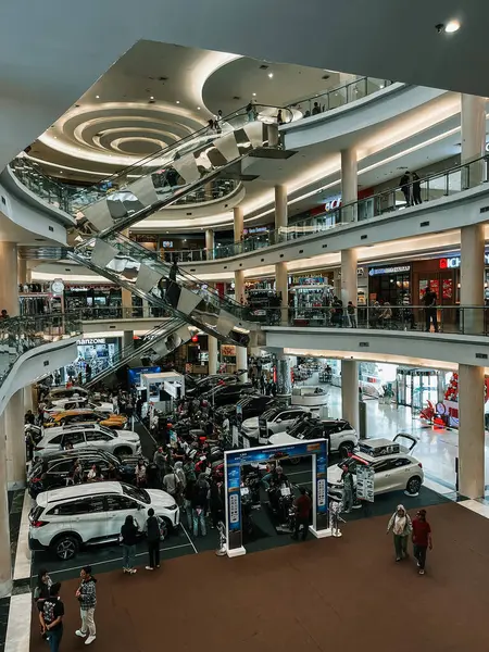 Çok katlı bir alışveriş merkezinde yürüyen merdivenleri ve araçları karıştıran insanları olan bir araba fuarı..