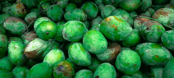 Doğal lekeleri olan taze yeşil mango yığınının yakın çekimi, canlı bir üretimdeki gösterişli doku, renk değişiklikleri ve tazelik..